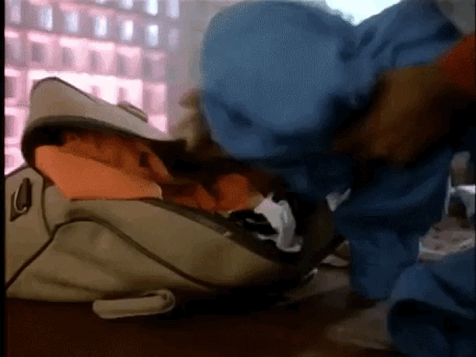 man shoving clothes into a bag with his foot